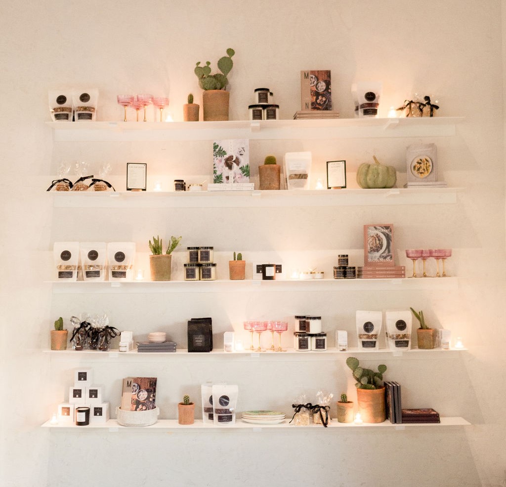 Amelia's market wall: white shelves of house granola, spice jars, candles and glassware