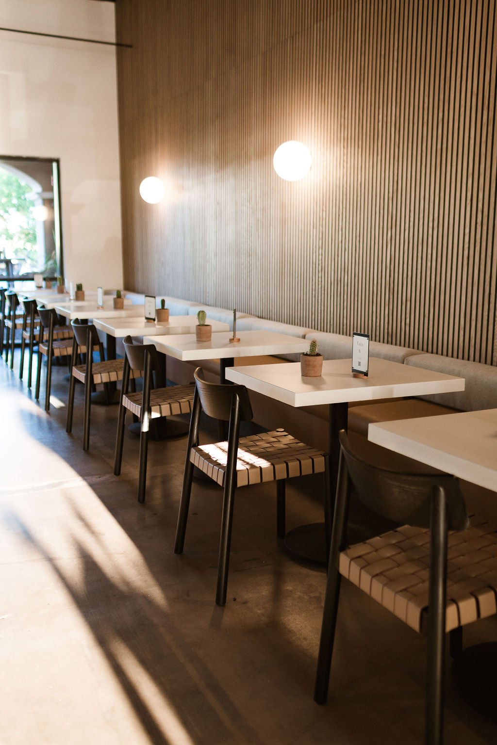 Amelia's dining room in the morning: white marble tables, woven chairs and globe lights along a slatted wood wall