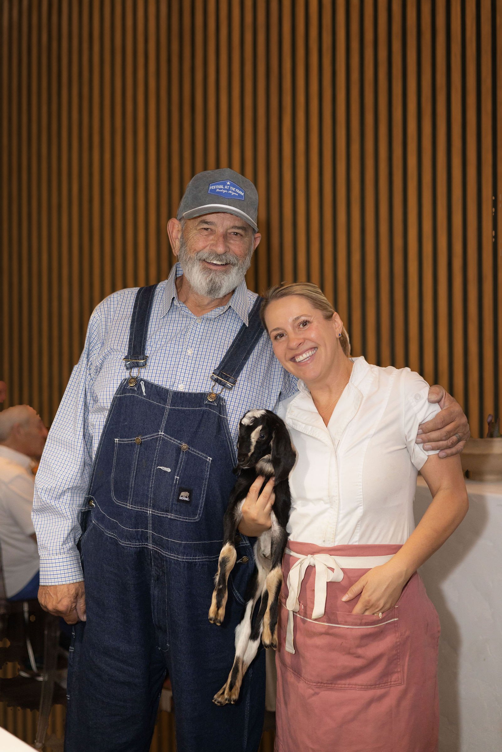 Chef Stacey with Wendell of Crowe Dairy, holding a baby goat at a Sunday Supper at Amelia's