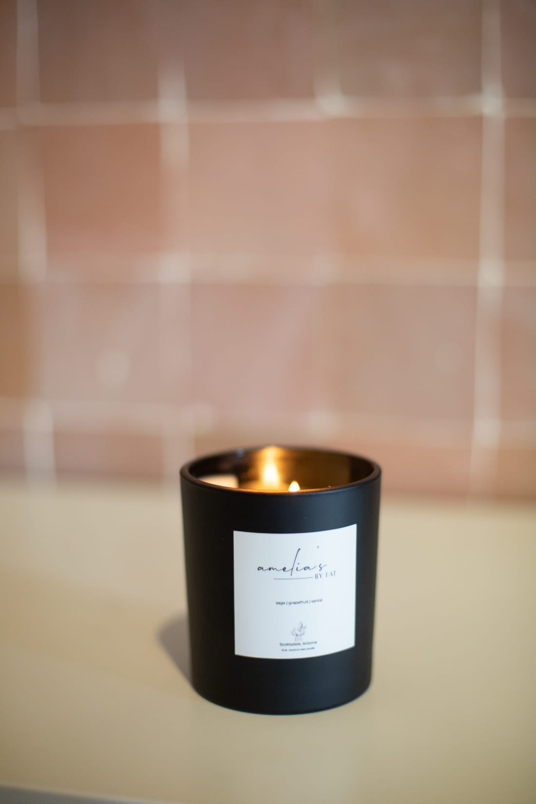 An Amelia's sage, grapefruit and santal candle burning on a counter