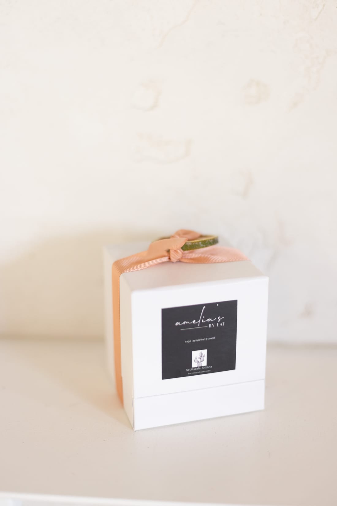 The boxed Amelia's candle on a shelf against a plaster wall