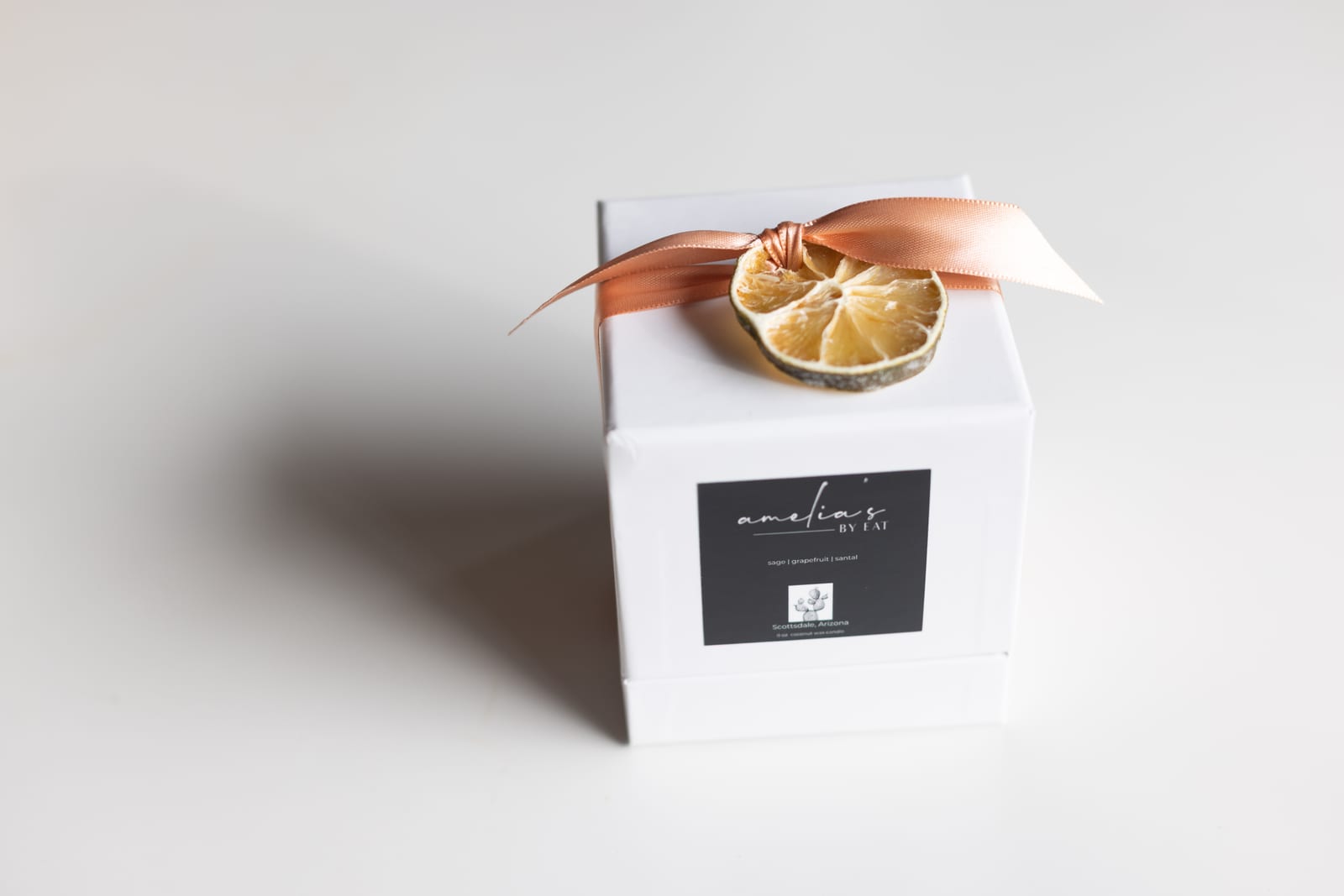 The small Amelia's candle in its white gift box, tied with a ribbon and a dried citrus slice