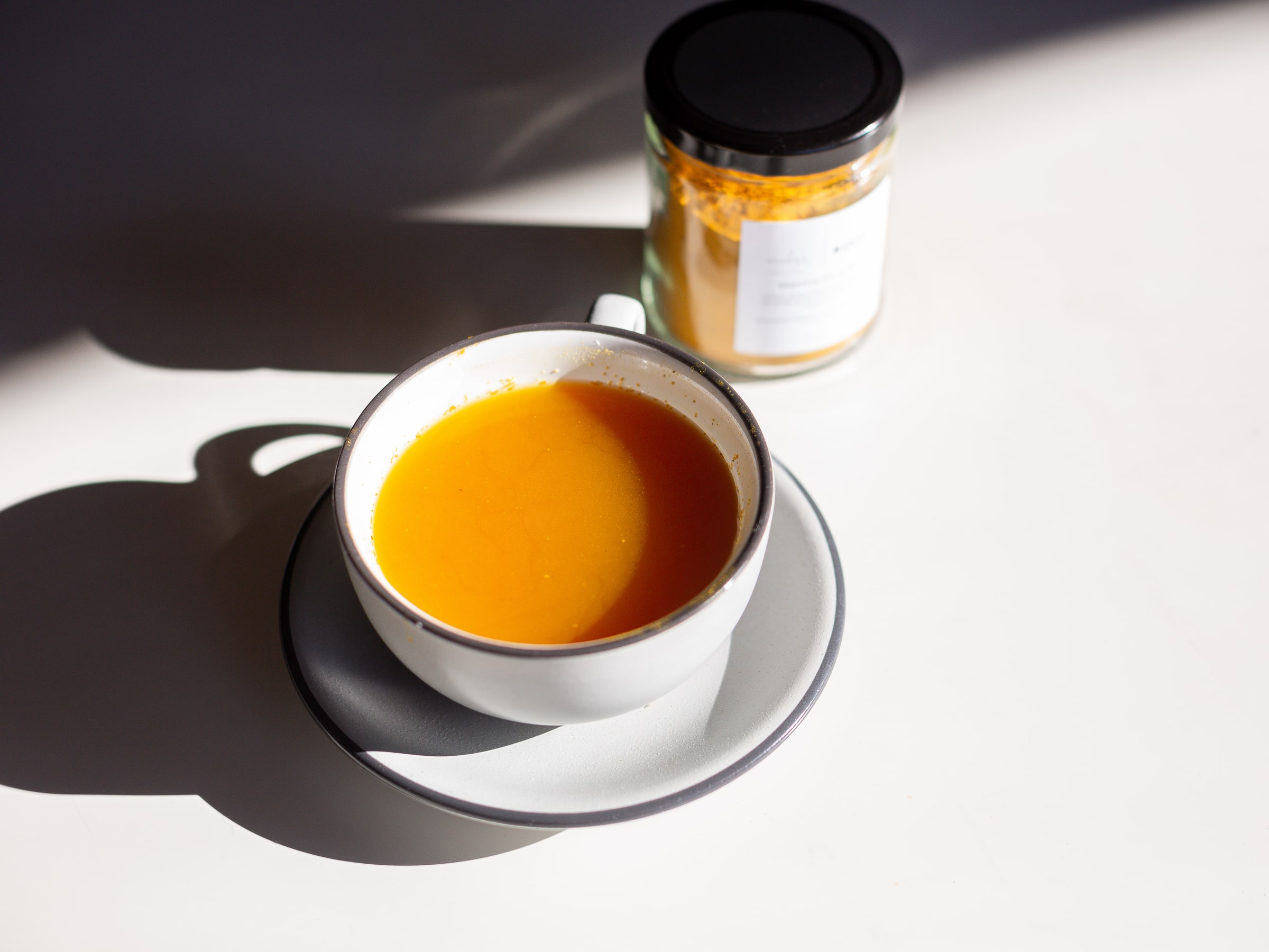 Morning Ritual Tea brewed in a white cup and saucer in morning light, the jar behind it