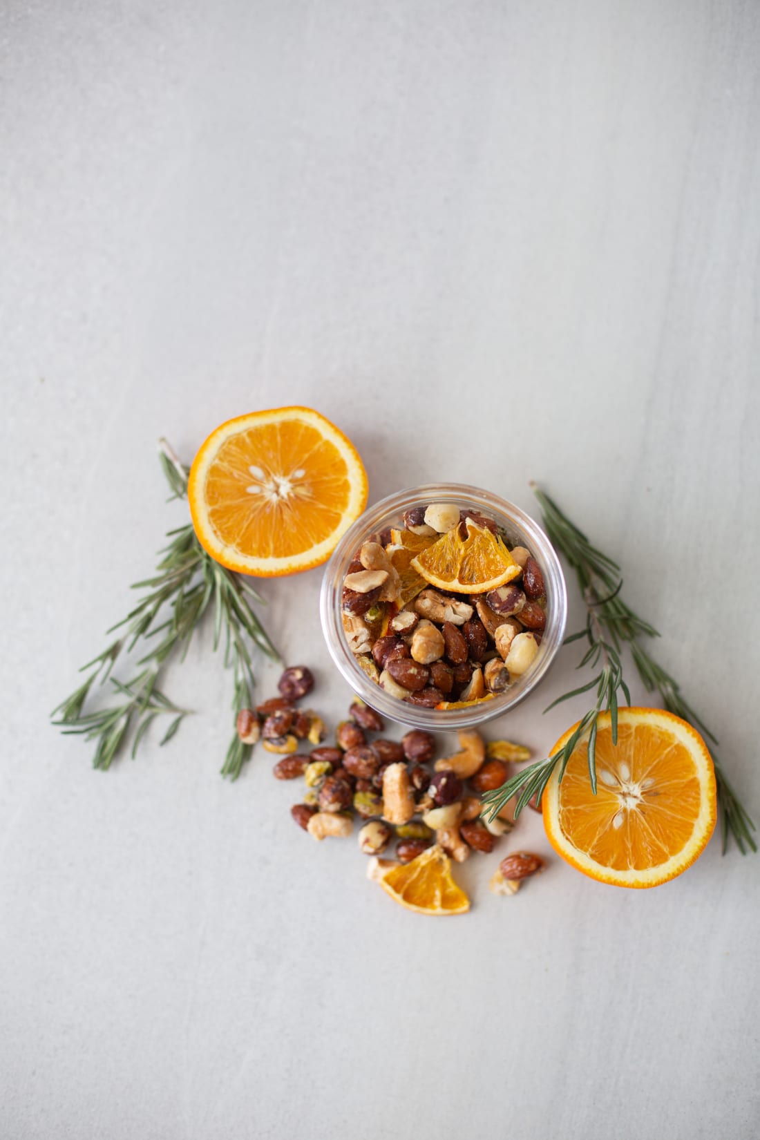 A jar of Amelia's spiced orange nuts from above, framed by orange slices and rosemary sprigs