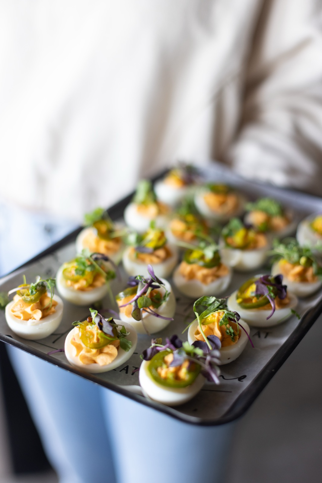 A tray of spicy deviled eggs topped with jalapeno and micro greens, carried out