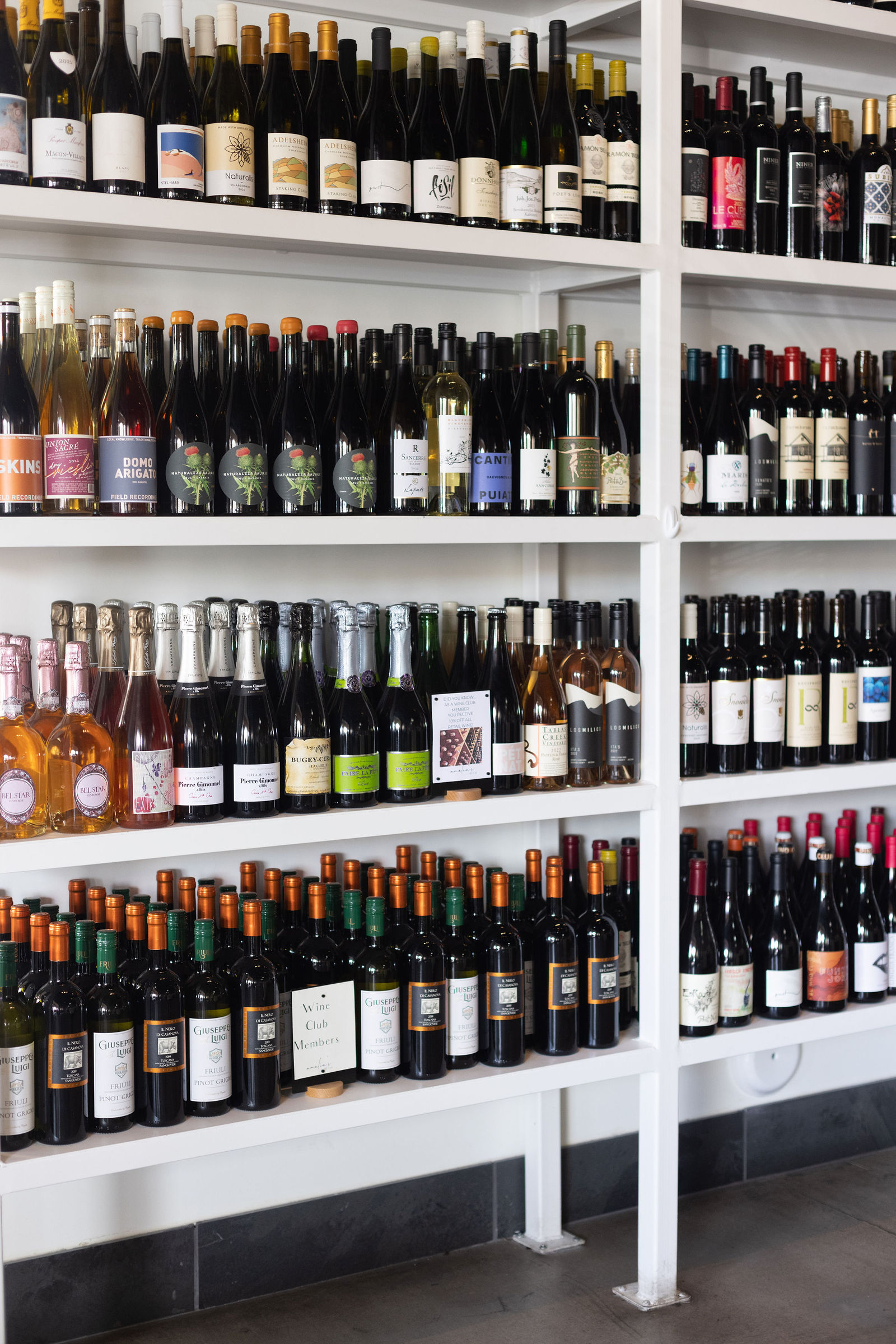Wine wall close up — white shelves packed edge to edge with bottles.