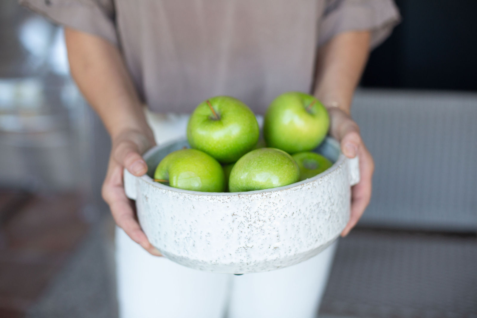Green apples in a white speckled stone bowl, held.