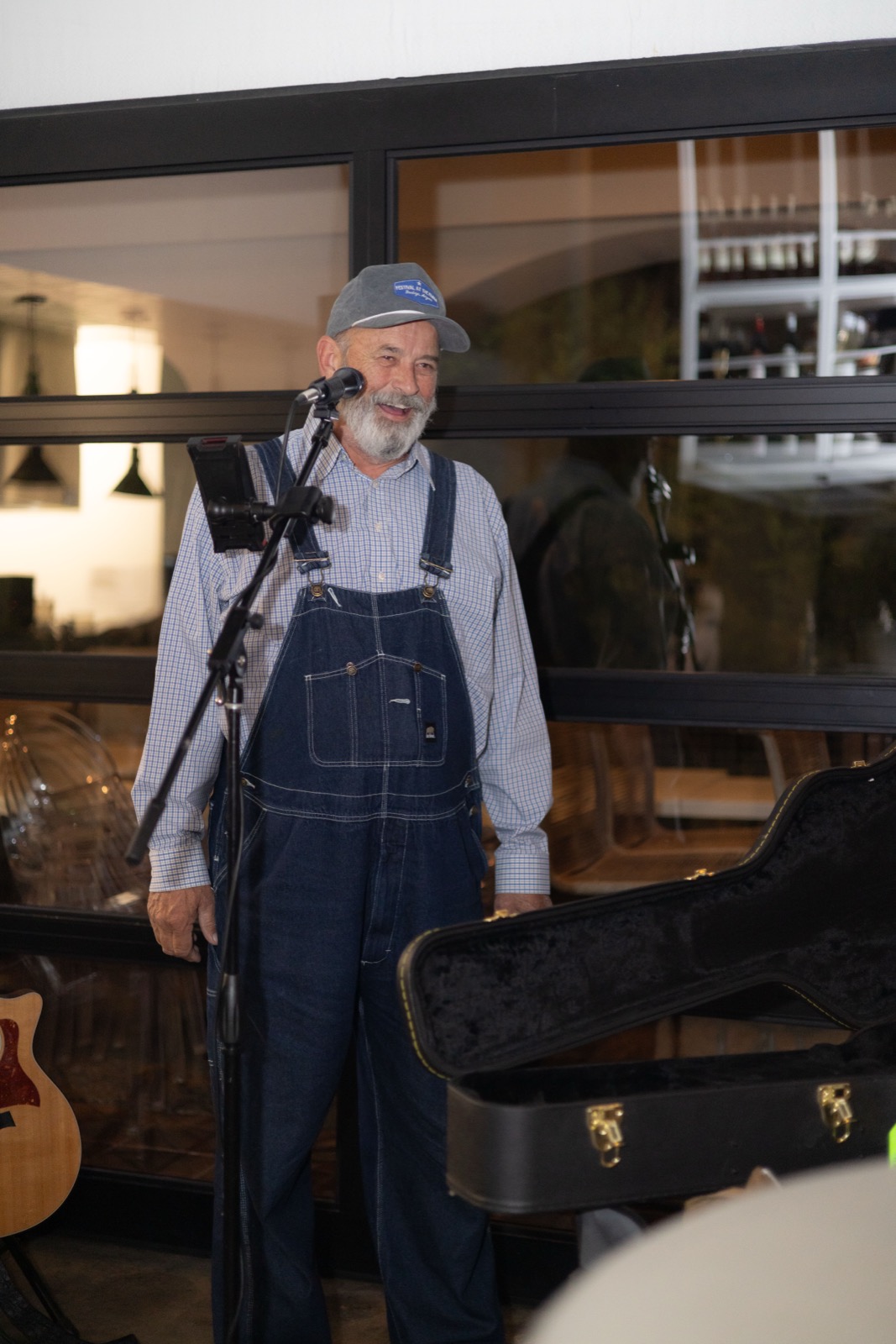 A grower in overalls speaking to the room between courses, an open guitar case at his feet