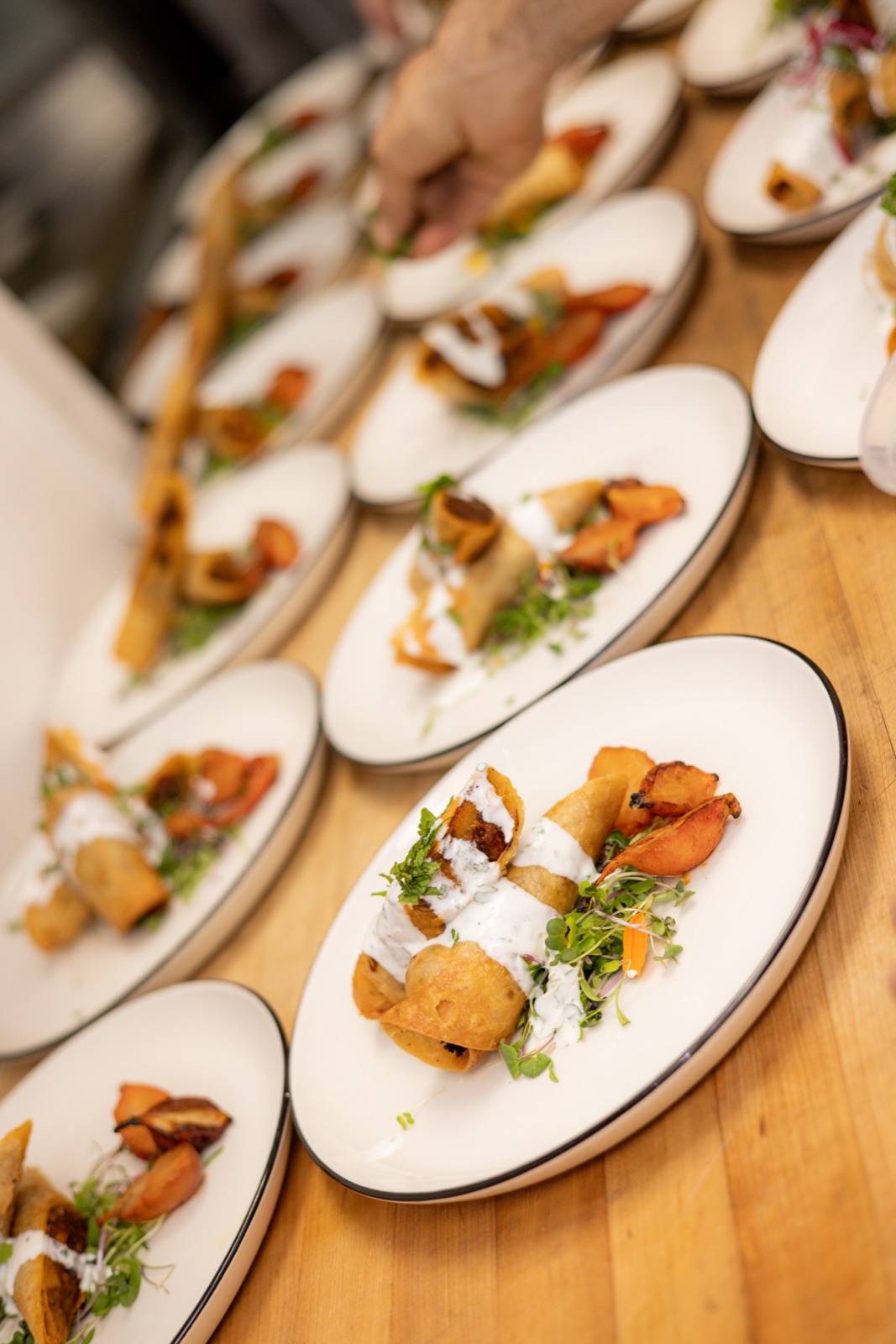 A row of plated courses being finished by hand with a garnish